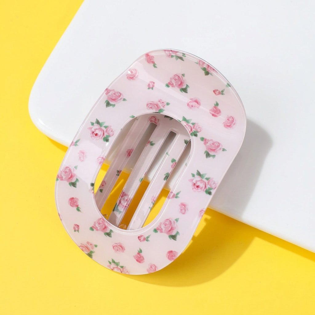 A translucent pink hair claw clip decorated with a pink rose and green leaf floral pattern, displayed on a split yellow and white background.