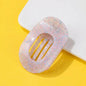 A translucent oval hair claw clip with a pink and light blue floral pattern, displayed on a bright yellow background with a white geometric prop. 